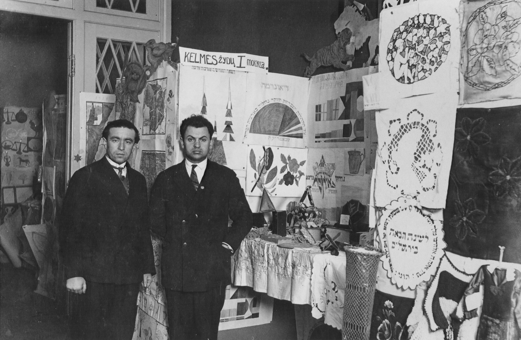 Two teachers from the Jewish Tarbut school in Kovno pose in front of a display of student artwork that was mounted in honor of the school's tenth anniversary.