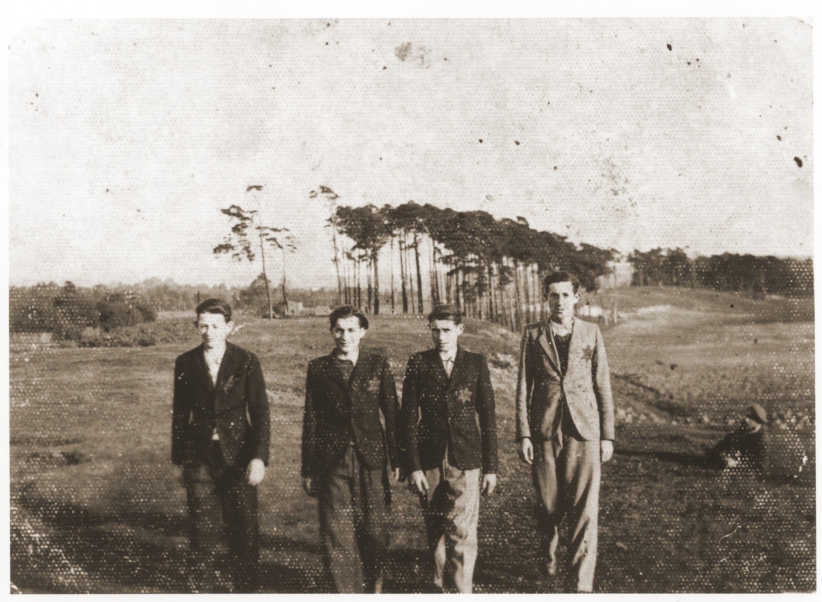 Four young Jewish men wearing yellow stars walk in an open field in the Strzemieszyce ghetto.

Pictured from left to right are Szmil Kohn, David Bajtner, Dawid Moszkowsi, and Aron Kohan.