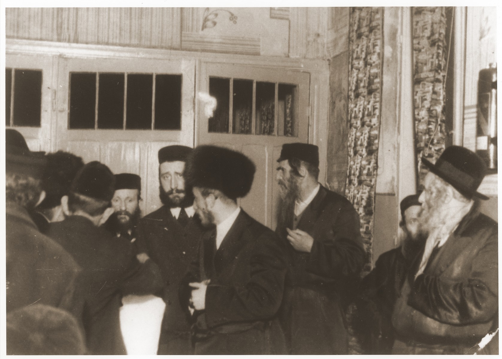 Ger Hasidim, including the rebbe, gather to greet  the bridegroom before a wedding.

Among those pictured are Abram Mordche Kopelman and Symcha Binem Alter.