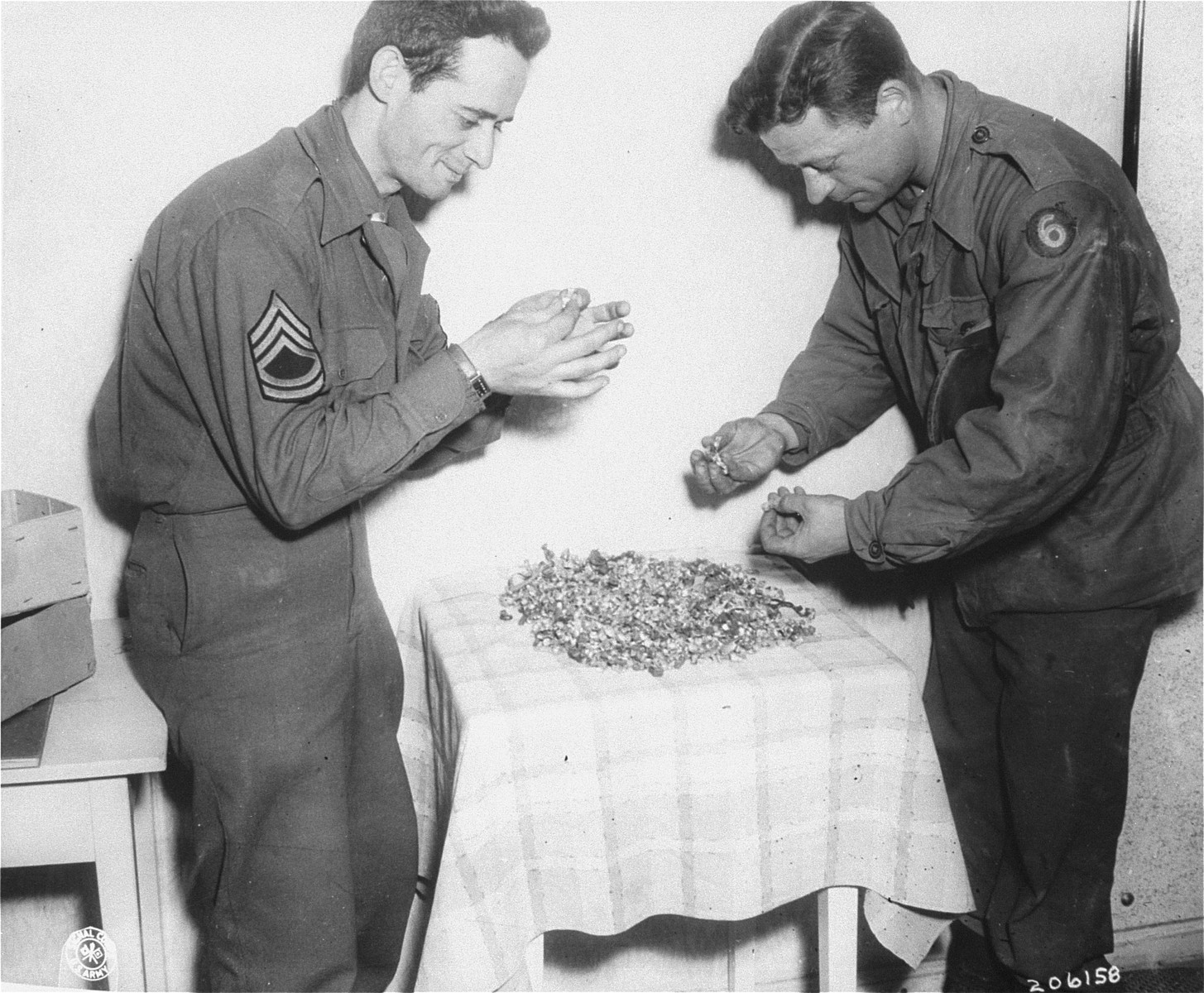 Tech Sgt. Claude L. Campellone (left) and Tech 4 Charles Henry look over the gold fillings that were found in Dachau.  The fillings were removed by the Germans when the prisoners died or were killed.