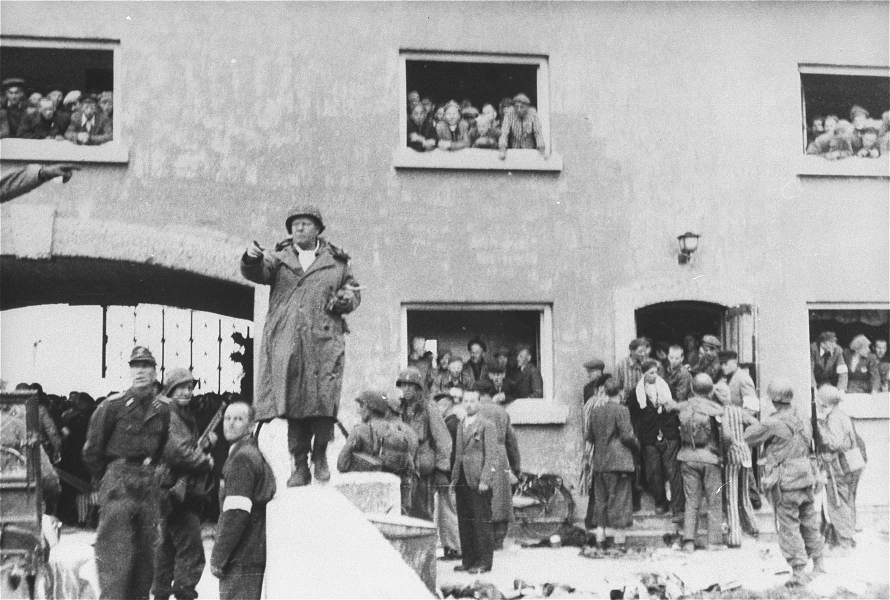 General Henning Linden, assistant commanding general, 42nd Rainbow Infantry Division, gives directions to his troops from the parapet of the bridge at the Jourhaus at the entrance to the Dachau concentration camp.

The civilian with the white armband is Dr. Victor Maurer of the ICRC (International Red Cross).  The German officer to the left is SS Lt. Wickert, the German officer who surrendered the camp. [oversize print]