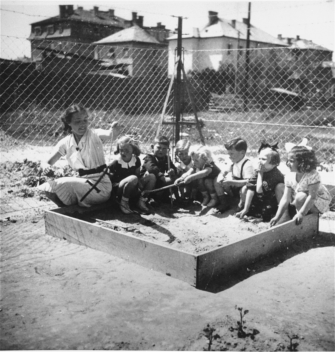 A group of Jewish and Hungarian children play with their teacher in a sandbox in the playground of a pre-school in Budapest.  

The pre-school was located on Tokoly Street in the 14th district.  Gyorgy Pick is seated third from the right.