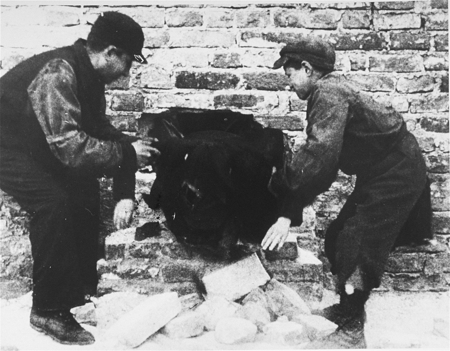 Two young smugglers pull a third through a hole in the ghetto wall.