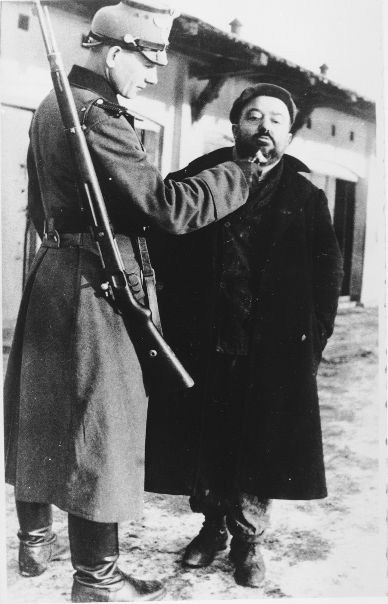 A German policeman publicly humiliates a Jew in the Zawiercie ghetto by shaving his beard.