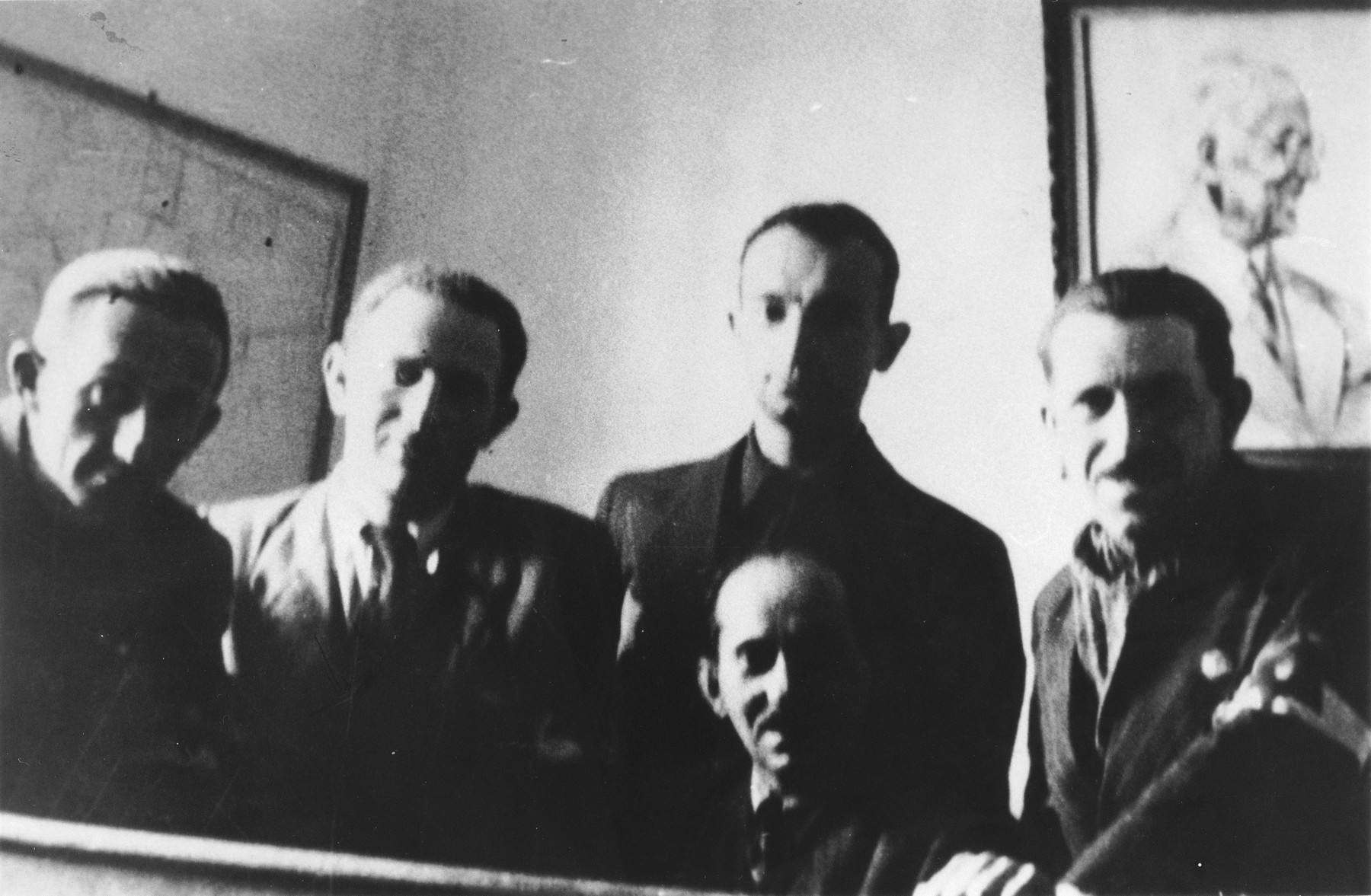 Four members of the Lodz ghetto leadership pose in an office beneath a portrait of Jewish council chairman Mordechai Chaim Rumkowski.