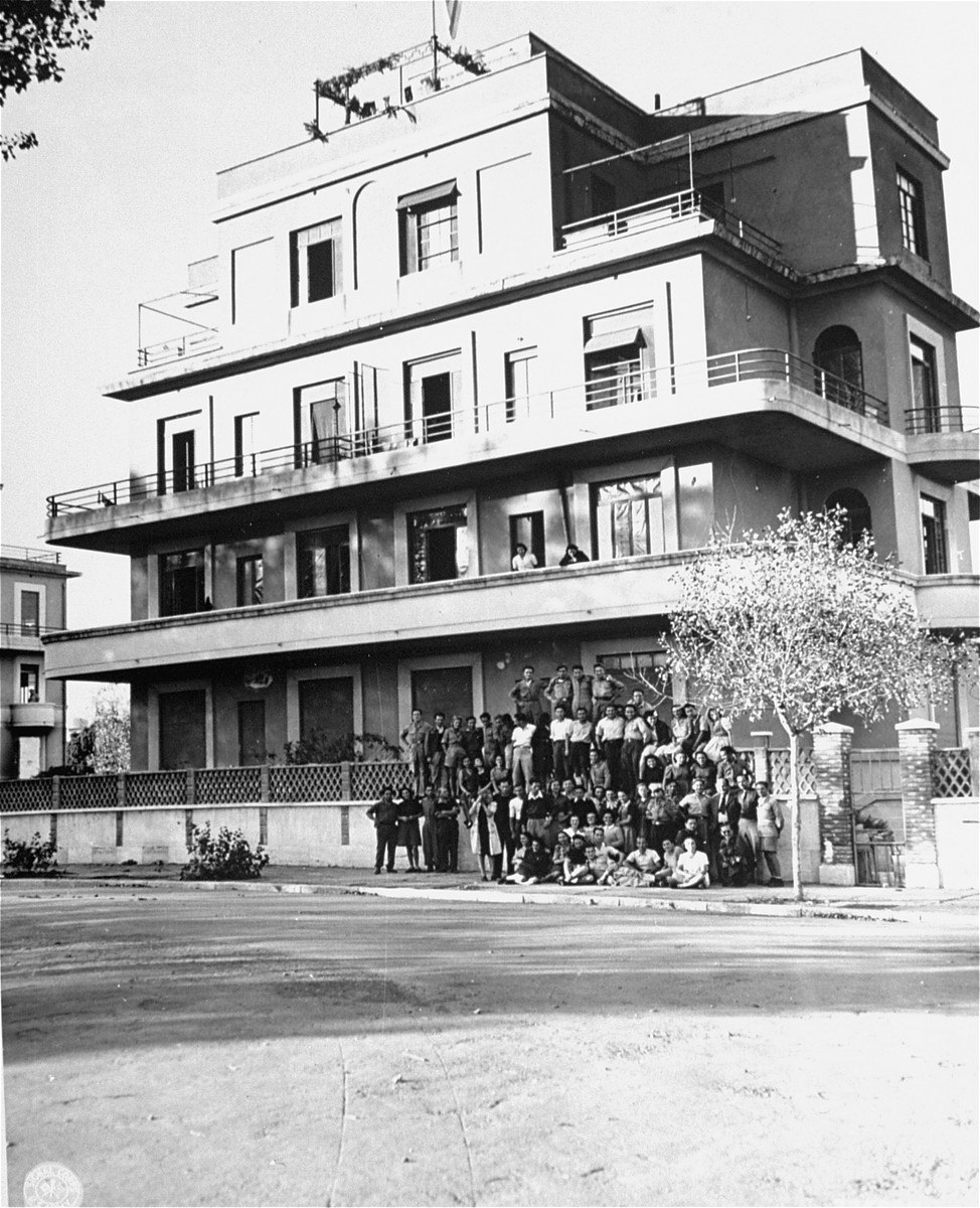 Group portrait of Jewish displaced youth in front of the villa in Rome where they are living.

The displaced persons center is being run jointly by the JDC (Jewish Joint Distribution Committee) and UNRRA (United Nations Relief and Rehabilitation Administration).  Among those pictured are Benjamin Brooks, a representative of the JDC, and Antonio A. Lovieri and Vlad F. Ratay, representatives of UNRRA.