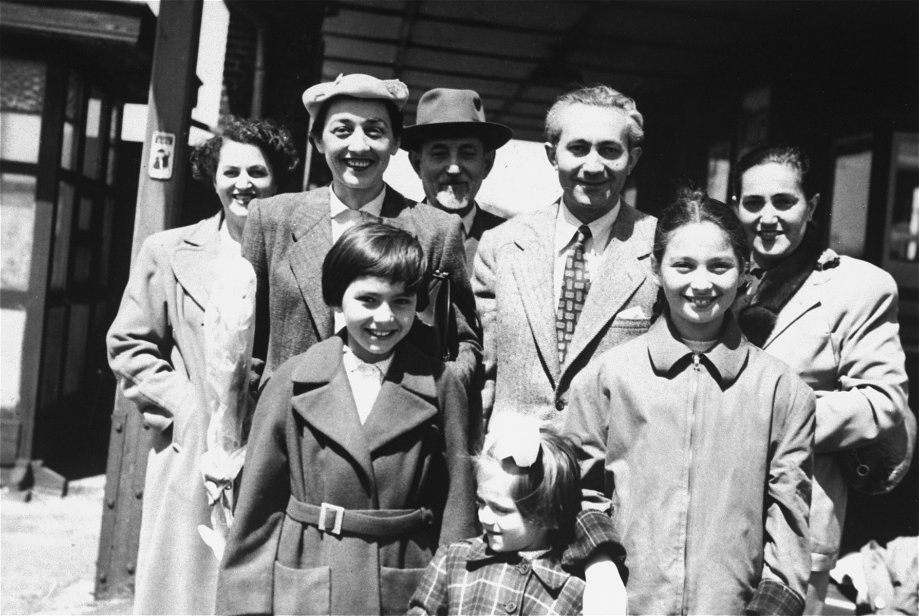 Group portrait of the Ament family at the train station in Antwerp prior to their departure for the United States.

Pictured are: First row, left to right are Jeanine Ament , Eleonore Ament and Miriam Matzner.  Back row (left to right):  Paula  Ament Schwalb, Mania Ament, Chaim-Shia Ament, Marian Ament and Rosia Ament Molkner.