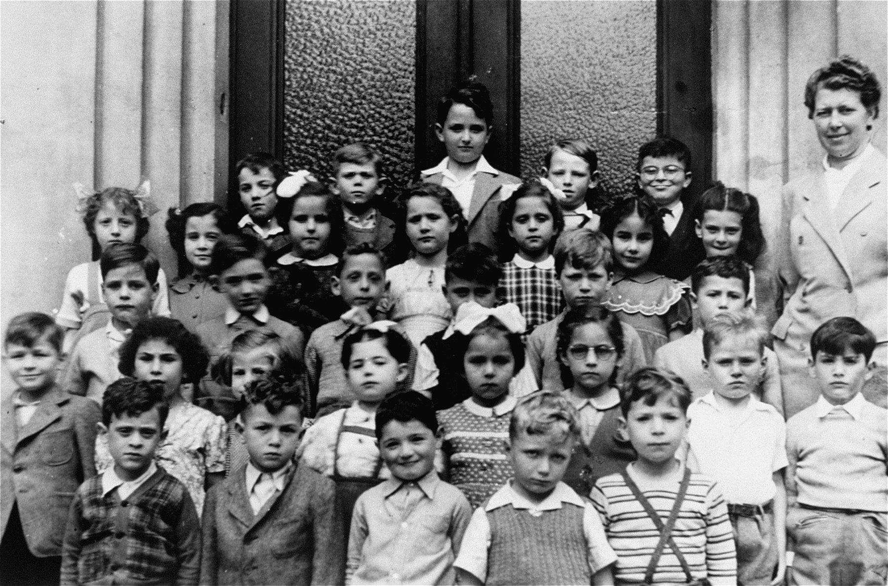 Group photo of the first grade class at the Tachkemoni Jewish private school in Antwerp.  

Jeanine Ament, is pictured in the second row from the front, fourth from the right.  The teacher is Mme Boucher.