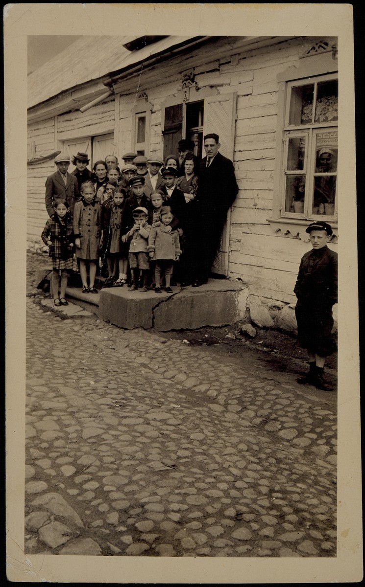 The Shlanski family poses on the steps of their home during a vist of the two Shlanski brothers Morris and Louis from America. 

Man standing at the far right is Isaac Shlanski and his wife Devorah is on his left.  The man with a beard in the back center is Avraham-Mordekhai Shlanski, father of Morris and Louis.  Fischl Shlanski (son of Rose and Zelig) is standing in the back at the far left. Second from left is Paike Shlanski Schwartz visiting from America.  Rose Shlanski is standing third from left with her daughter Hayya in front of her.