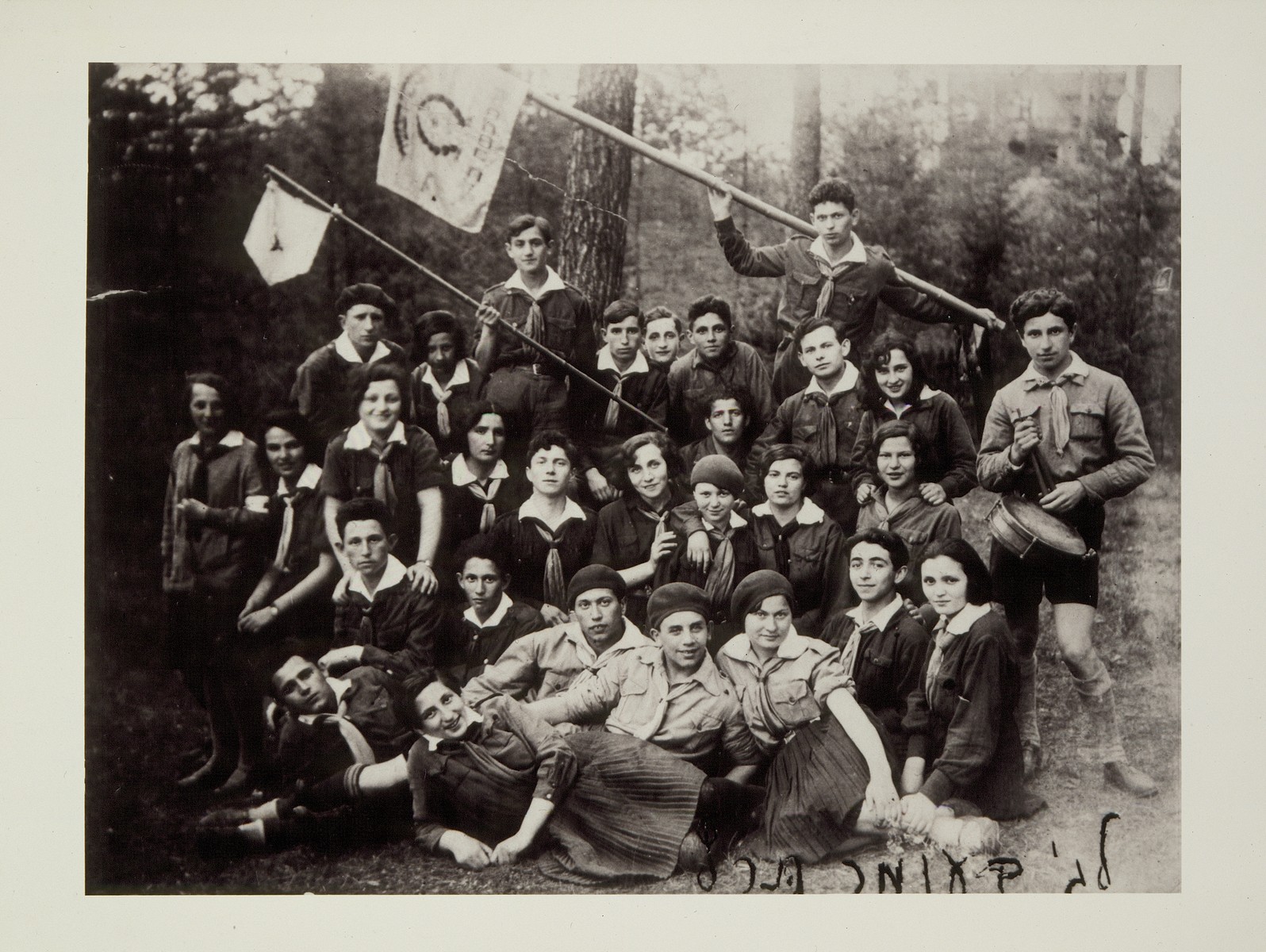 Members of Hashomer Hatzair from Eisiskes and Vilna celebrate Lag Ba'Omer on an outing in the woods. 

Dov Wilenski, is standing in the top row holding a flag.  He later immigrated to Palestine.  Pictured in the center of the second row, wearing a beret, is Resia (nee Gurwicz) Alpert,  from Vilna.  She immigrated to Palestine (Kibbutz Amir) in 1939.