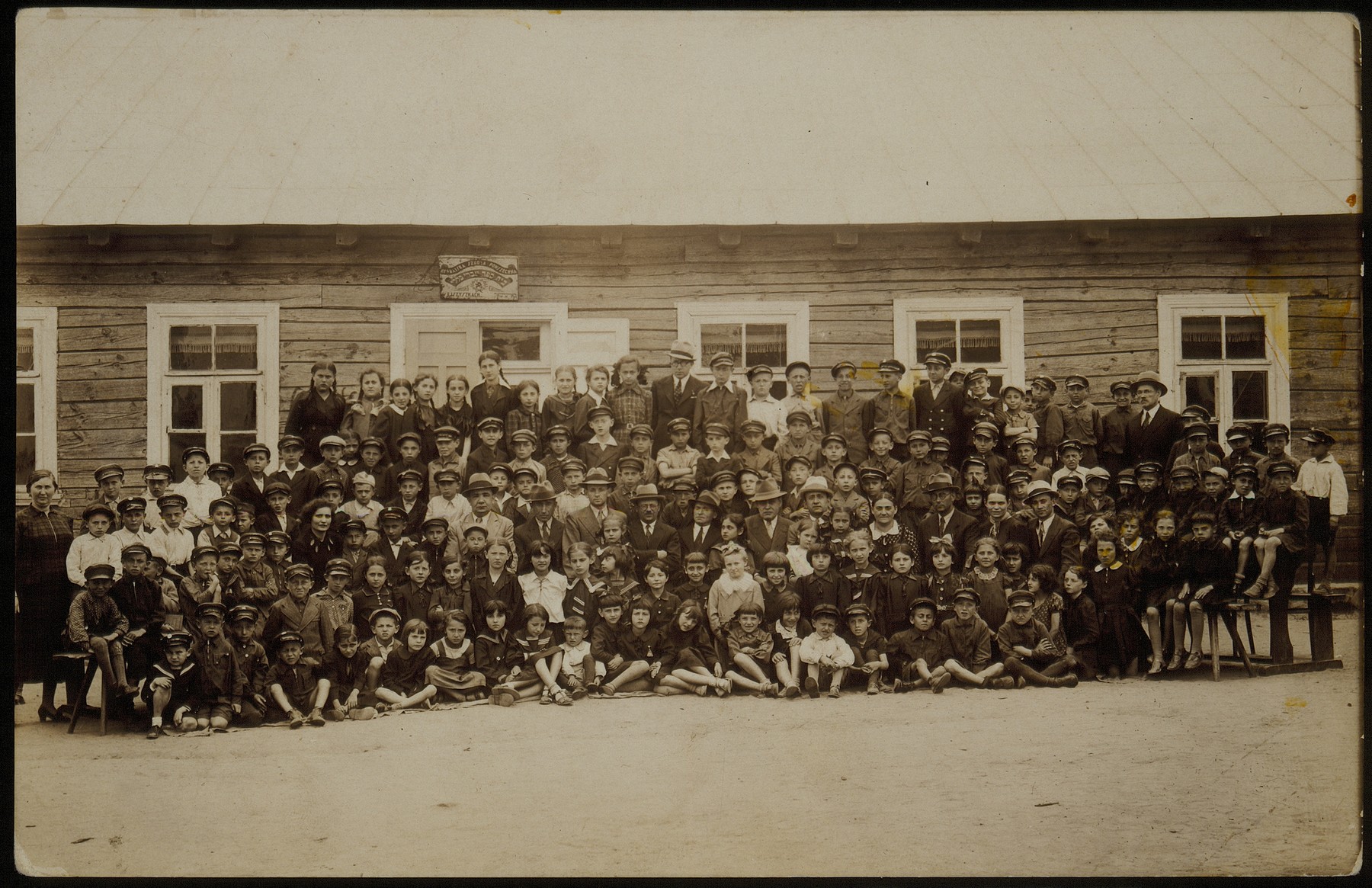 Students and faculty of the Eisiskes Hebrew school pose for a group portrait with members of the Education Committee in honor of Philip Shlanski's visit from America and his contribution to the school.

Sitting among the adults (fourth from right) Miriam Kaganowicz. The teacher standing at the far right is Shaul Michalowski. The teacher in the back row is Okun. Top row far right is Shaul Lidski, (7th from right) Liebke Kaganowicz, (9th from right)  Avigdor Katz, (10th from right) Zelig Ballon.  Second row from top, from left to right: 9th boy: Moshke Dubachnky, 6th  boy: Moshe Edelstin, 14th boy: Moshe Baskunski, 17th boy: Elisha Koppelman and 24th boy Reuvan Piakowski.  Third row from bottom from left to right: Alte Katz, President of Education Committee, 3rd boy: Benyamin (Niomke) Sonenson, Meir Rosenbloom, a member of the Education Committee sitting to the right of light-suited man and to his right is Nachum Koppelman, a member of the Education Committee.  Man on her right is David Schwartz. At the far right is the teacher,Belsky.  

Except for Liebke Kaganowicz and Reuvan Piakowski, most of the others pictured perished during the Holocaust.