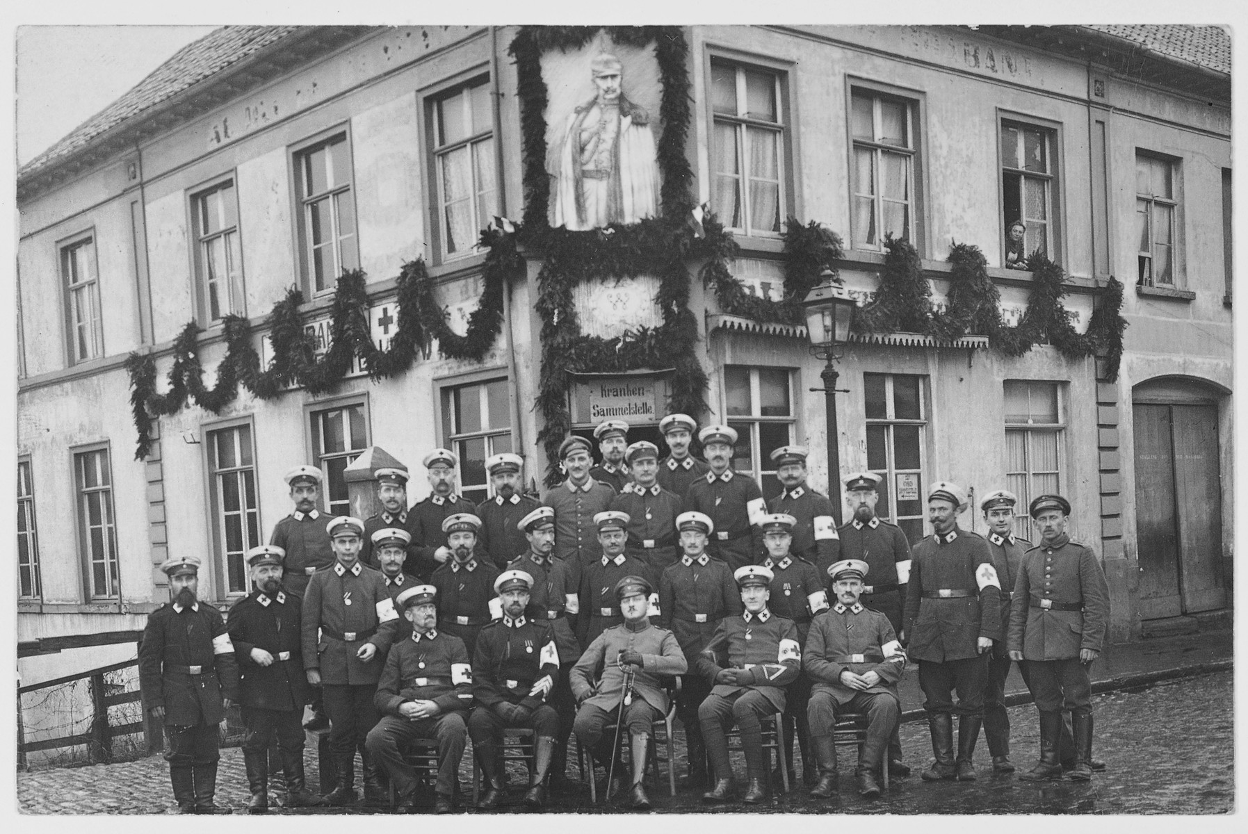 Group portrait of doctors who have been mobilized for the war effort, beneath a portrait of the Kaiser outside a hospital.