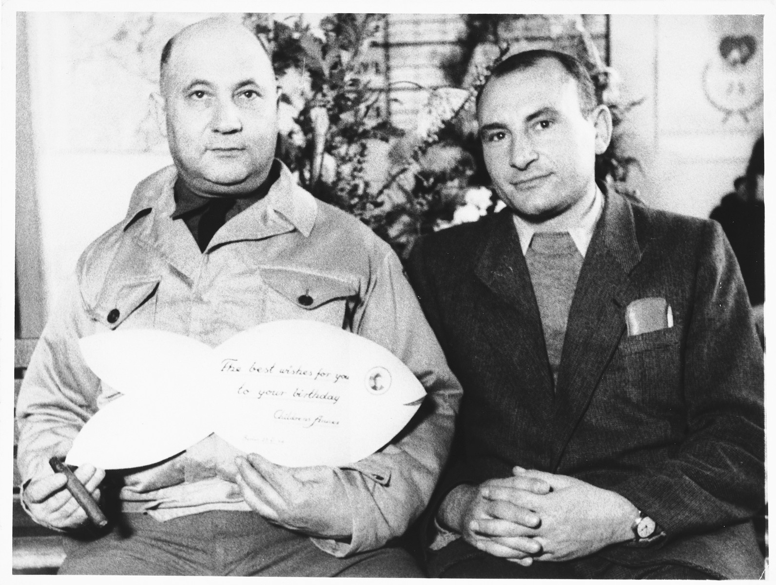 UNRRA camp director, Harold Fishbein (left), holds up a birthday card shaped like a fish, which he received from the children in the Schlachtensee displaced persons camp.

Pincus Proszowski (later Peter Prosaw) is pictured on the right. A survivor of the Lodz ghetto and Auschwitz, he was the director of the Schlachtensee children's home and the graphic designer who made the camp scrapbook.