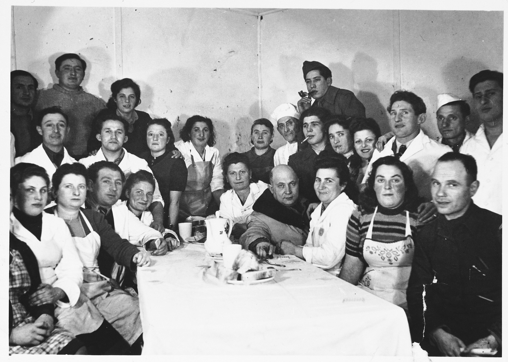 Group portrait of Jewish DPs gathered around a table in the Schlachtensee displaced persons camp.
