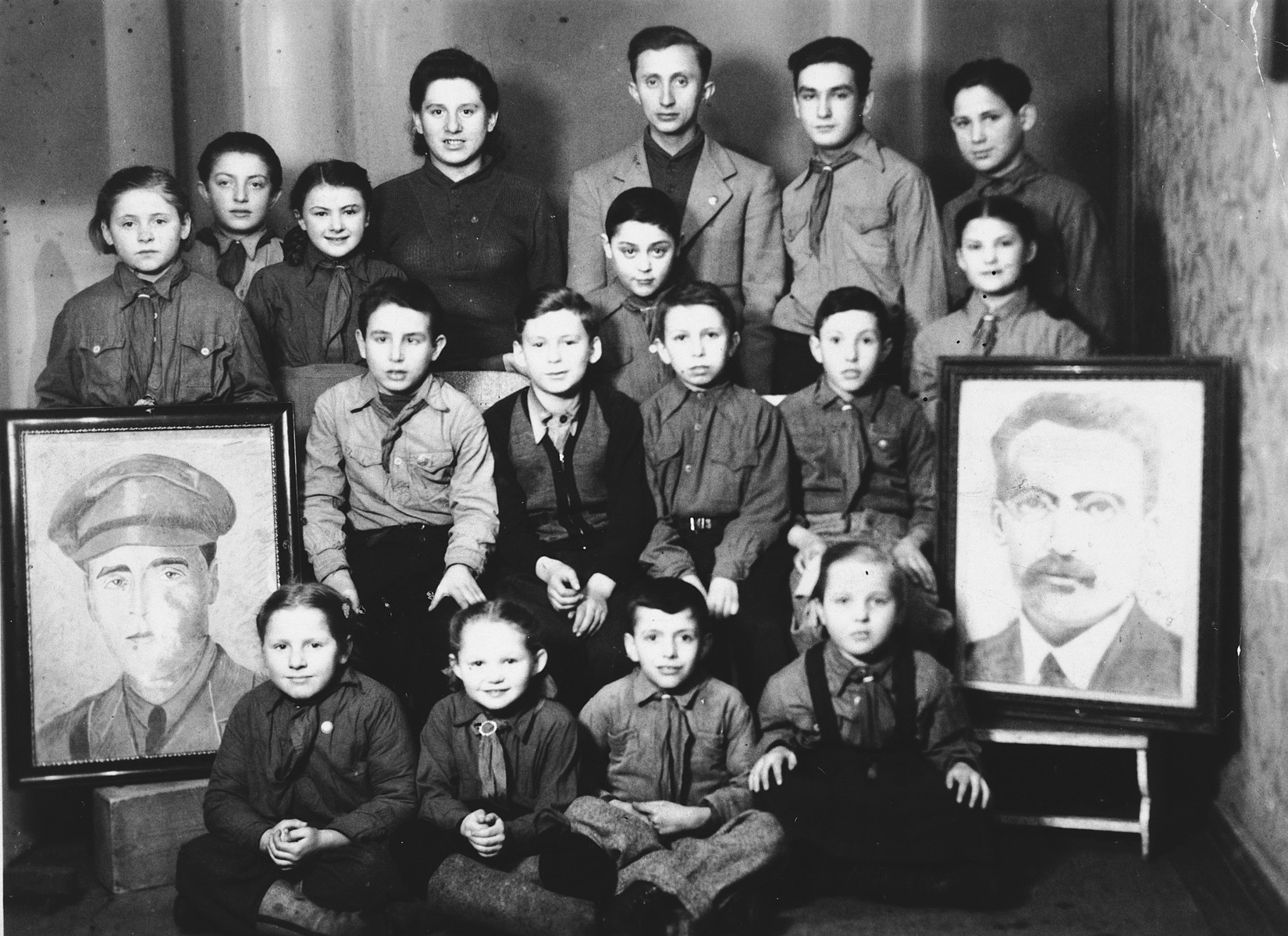 Children belonging to the Zionist  youth movement Dror in Poland pose between portraits of two Zionist heroes, Joseph Trumpeldor and Ber Borochov.

Among those seated on the floor is Leah Szain.
