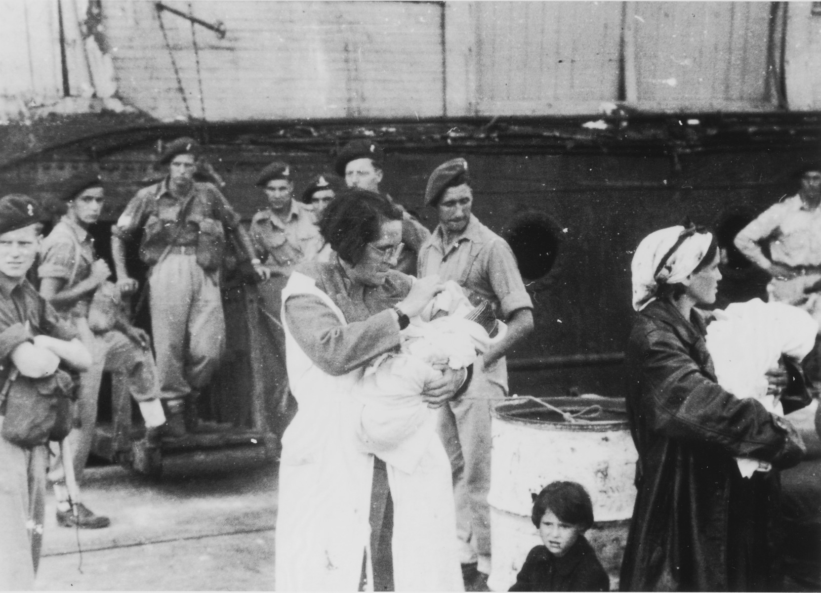 Two female passengers of the Exodus 1947 wait on the dock in Haifa holding infants who were born during the voyage.  

The woman at the left is the grandmother of the infant she holds.  The child's mother died in childbirth.