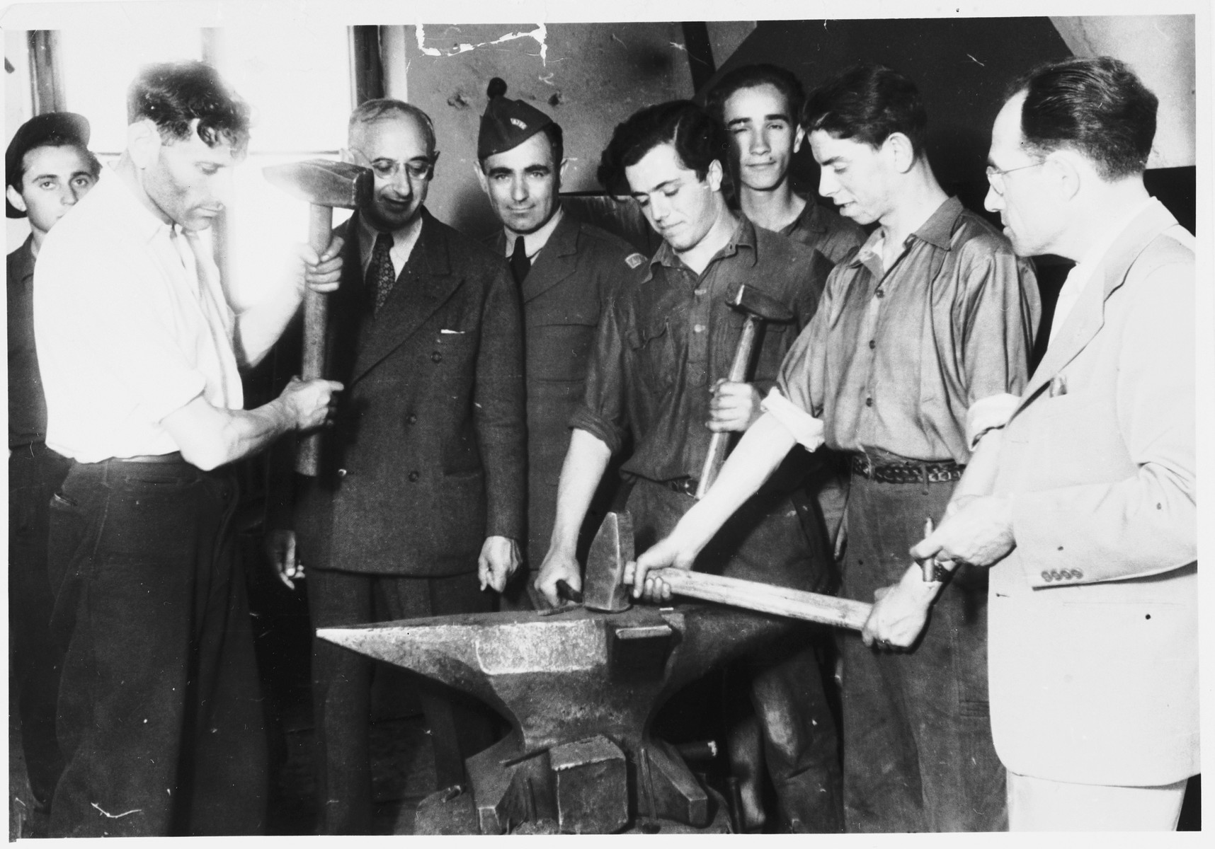 Issak Libstug, wearing his AJDC uniform, watches men demonstrate the use of an anvil in a workshop in the Foehrenwald displaced persons camp.