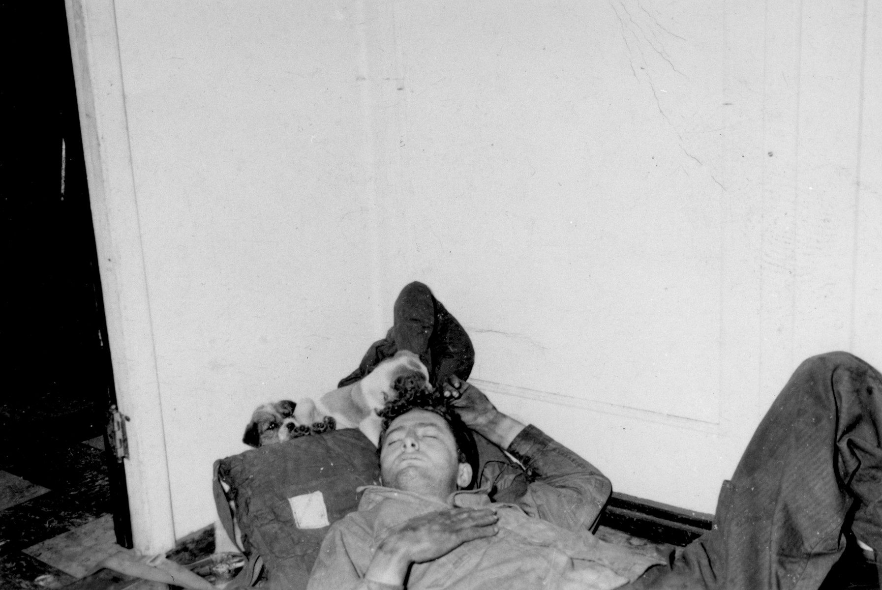An exhausted crewman sleeps on the floor of a room on the President Warfield after the gale that nearly sank the ship during its first attempt to cross the Atlantic Ocean. 

The ships mascots, two puppies, are curled up near his head.