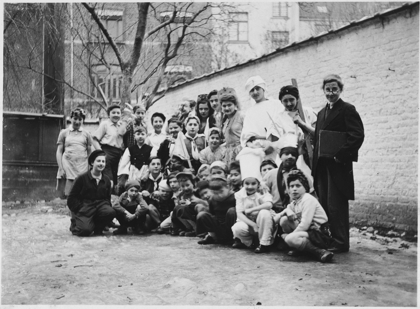 Group portrait of Jewish refugee children dressed in Purim costumes at the Orphelinat Israelite de Bruxelles children's home on the rue des Patriotes.

Among those pictured are: Walter Mendler, Binchen Gelbart, Emmanuel Trattner, Rolf Apt, Rachel Kirschbaum, Albert Tennenbaum, Edith Grunbaum, Herbert Kessler, Menachem Somer, Schmuel Amsel, Bessie Sturm, and Helga Somer.