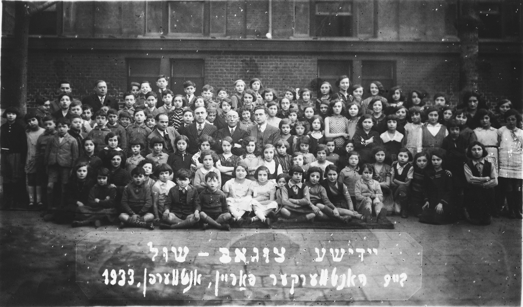 Group portrait of the children and faculty of the Yiddish Tsugob shul, sponsored by the Jewish Artisan Association.

Among those pictured is Paula Lasman (second row, far left), Mr. Schwartz (in the group of men in the center, far left), Mr. Lubka (back row, far left).  Both men were on the board of the Tsugobshul.
