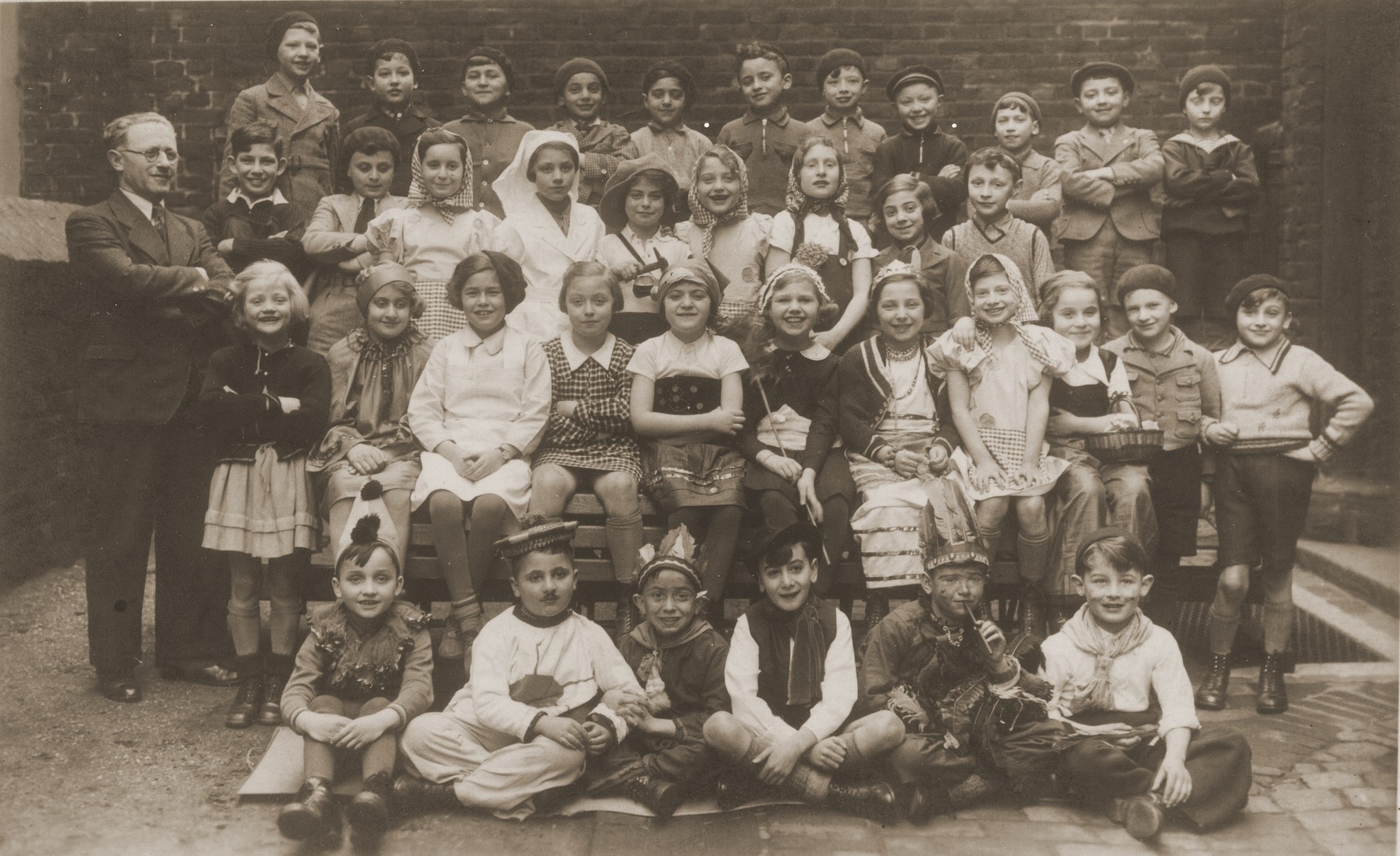 Group portrait of students at the Israelitische Volkschule Essen dressed up in Purim costumes.  

Among those pictured is the teacher, Fritz Kaiser, (standing at the left), and Heinz Straus (front row, fourth from the left).