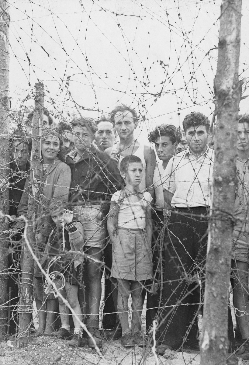 A group of former Exodus 1947 passengers stand behind the barbed wire enclosure at the Poppendorf displaced persons camp in Germany.