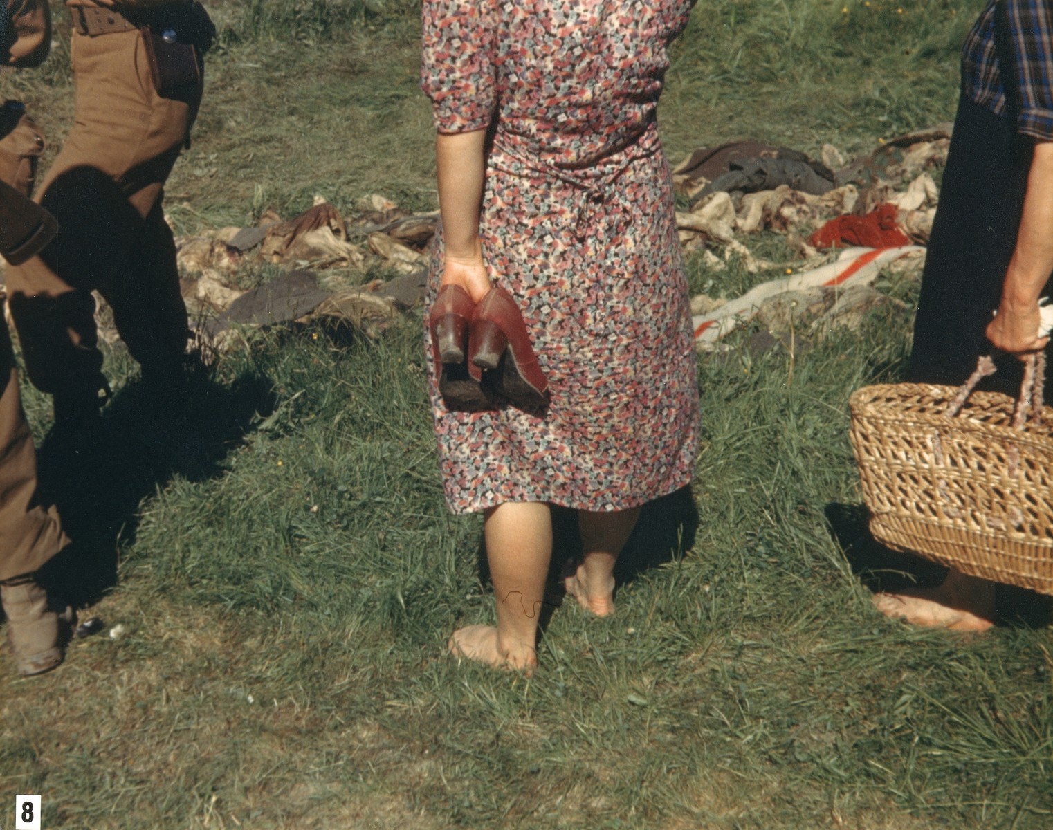 Bare-footed German women from Nammering look at the corpses of prisoners exhumed from a mass grave near the town.  

[The women might have been forced to take off their shoes by U.S. troops so they would walk through the mud near the grave.]