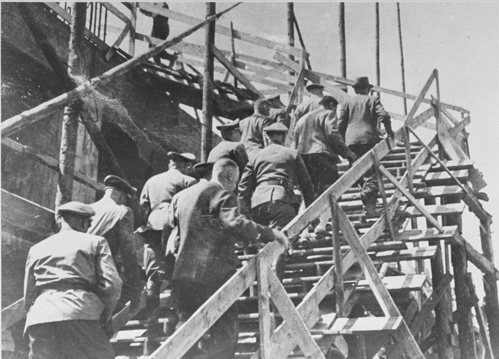 Reichsfuehrer SS Heinrich Himmler (top left) climbs a wooden staircase during a tour of the Monowitz-Buna building site in the company of Max Faust (top right). 

Faust, who was an IG Farben engineer, was the head of building operations at Monowitz-Buna.