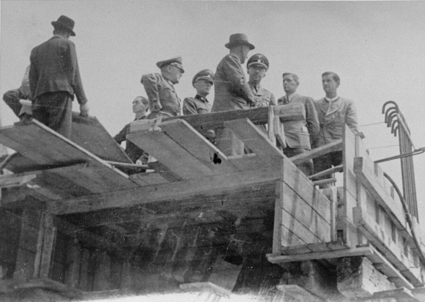 Reichsfuehrer SS Heinrich Himmler converses with Max Faust (wearing the fedora) on the upper floor of a partially constructed building, during a tour of the Monowitz-Buna building site. 

Faust, who was an IG Farben engineer, was the head of building operations at Monowitz-Buna.