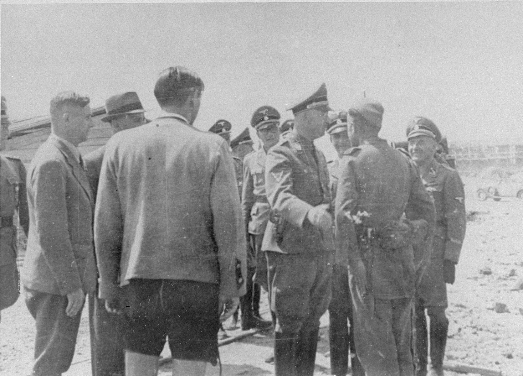 During a tour of the Monowitz-Buna building site, Reichsfuehrer SS Heinrich Himmler speaks to a member of the SS who is supervising the prisoners working on the construction of the IG Farben plant.
