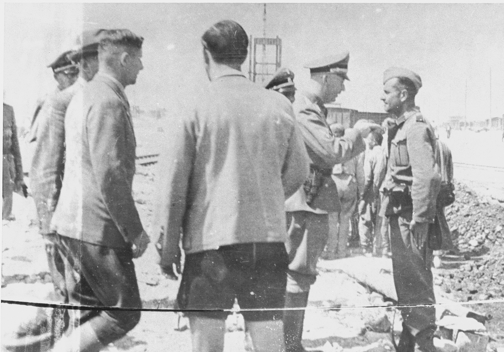 During a tour of the Monowitz-Buna building site, Reichsfuehrer SS Heinrich Himmler speaks to a member of the SS who is supervising the prisoners working on the construction of the IG Farben plant.