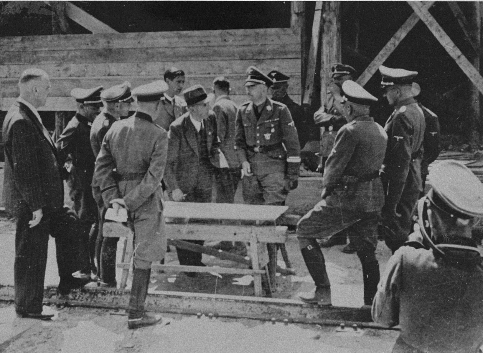 Reichsfuehrer SS Heinrich Himmler converses with Max Faust (wearing the fedora) while looking at a building plan during a tour of the Monowitz-Buna building site.

Faust, who was an IG Farben engineer, was the head of building operations at Monowitz-Buna.