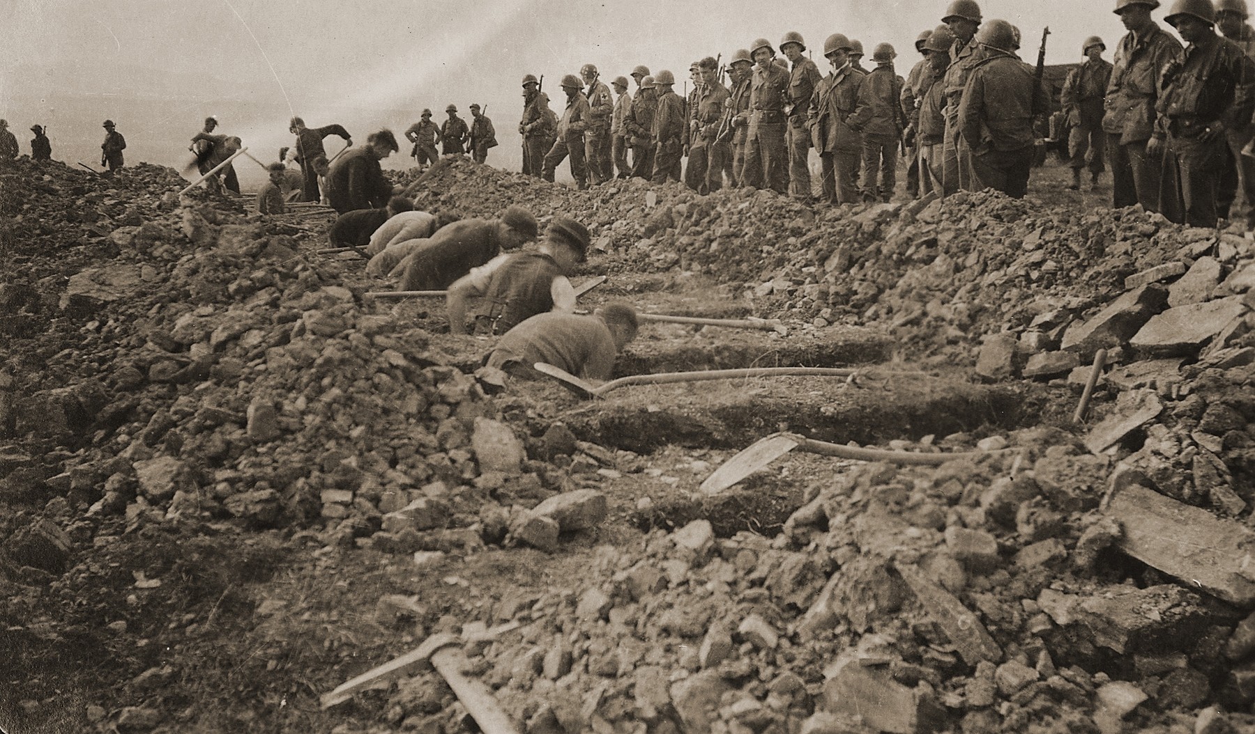 American troops look on as German civilians from nearby towns dig graves for corpses found in the Ohrdruf concentration camp.