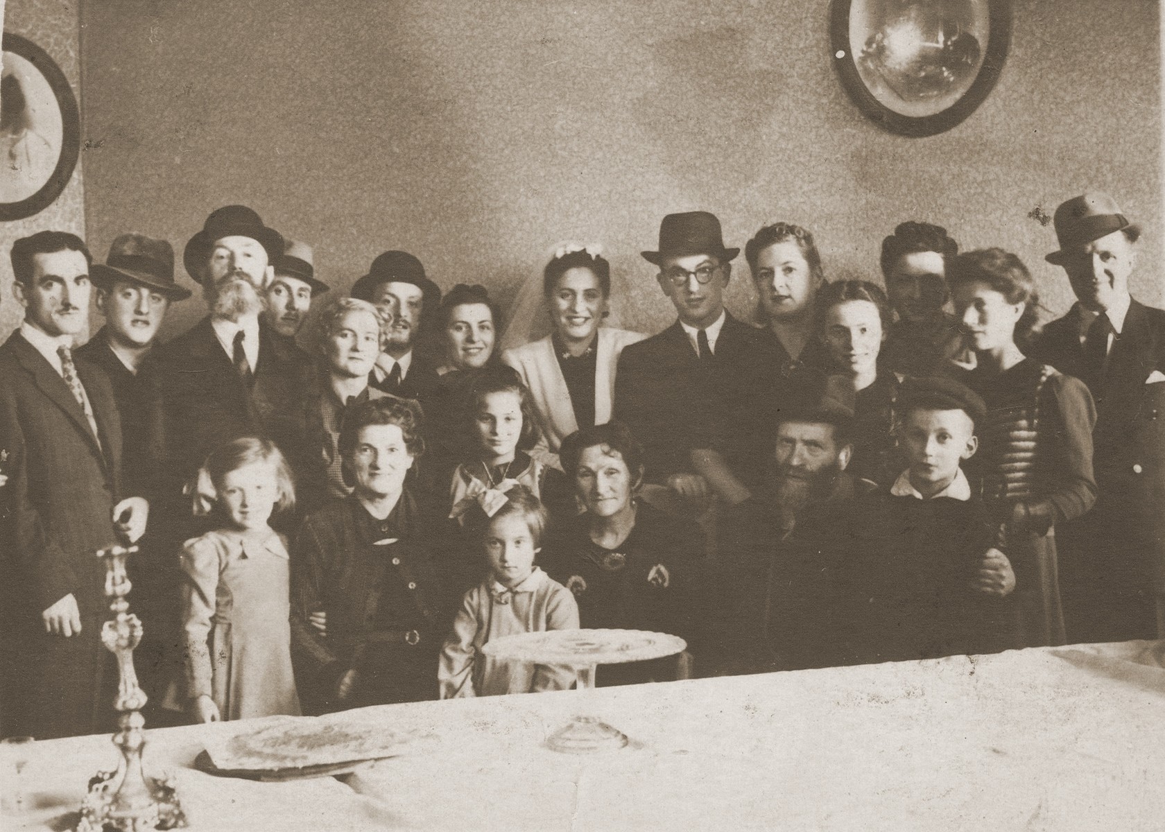 Group portrait of family and friends at the wedding of Hanka Rechtleben and Ignac Frank, the donor's maternal uncle.  

This picture was sent to Szmuel Icek Rotsztajn in Vilna.

Standing from left, in the back row are: Chaim Frank; Luzer Eliezer Frank; Naftali Frank (the donor's maternal grandfather); Mietek Leibhaber; Golda Lieba Frank Rotsztajn (the donor's mother); Froim Frank; Sala Mendelsohn Frank (from Zgierz); Hanka Rechtleben (the bride); Ignac Frank (the groom); Itka Frank (Chaim's wife); Reginka Rotsztajn (the donor's sister); Pola Frank; Roma Rotsztajn (the donor); and Mietek Pressburger.  In the front row, from left to right are: Rutka Frank (daughter of Froim and Sala); Chava Frank (the donor's maternal grandmother); Justynka Rotsztajn (the donor's sister); Gela Frank (the daughter of Itka and Chaim, below Justynka; Dwora Rotsztajn (the donor's paternal grandmother); Mordechai Nissan Rotsztajn (the donor's paternal grandfather); and Dawidek Rotsztajn (the donor's brother).