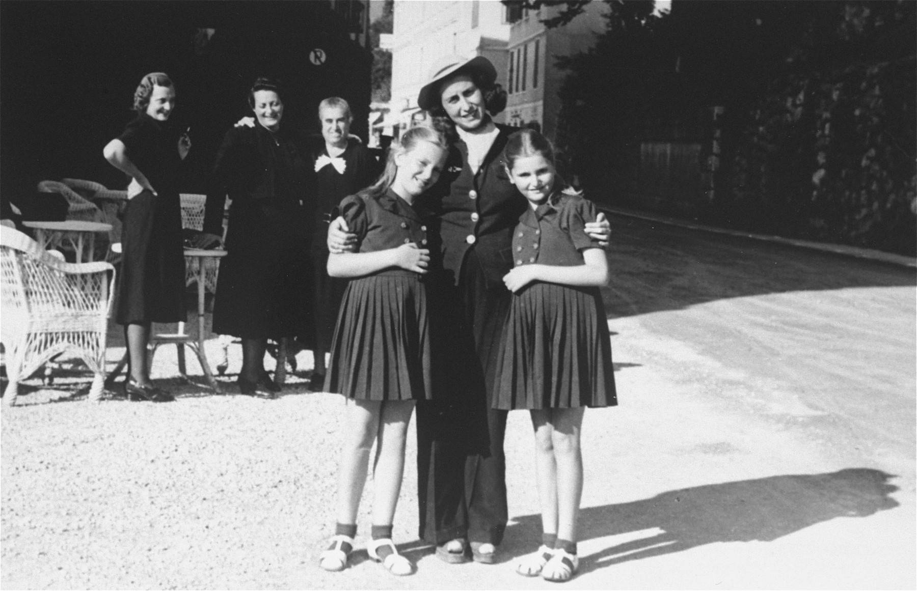 Dolly (left) and Mari Dezsoefi pose with their cousin, Dorothea (Babi) Halberg.  

In the background are Johanna Selinger, the twins' mother, standing far left, her sister, Elizabeth Tieberger, center, and family friend, Mrs. Diamant.