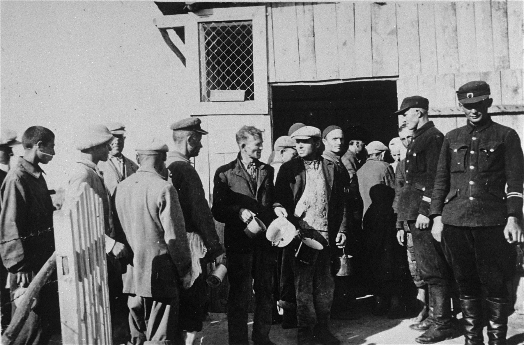 Two camp guards supervise a group of Jewish forced laborers from the Wisznice ghetto while they stand in line for food at the Horodyszcze labor camp.