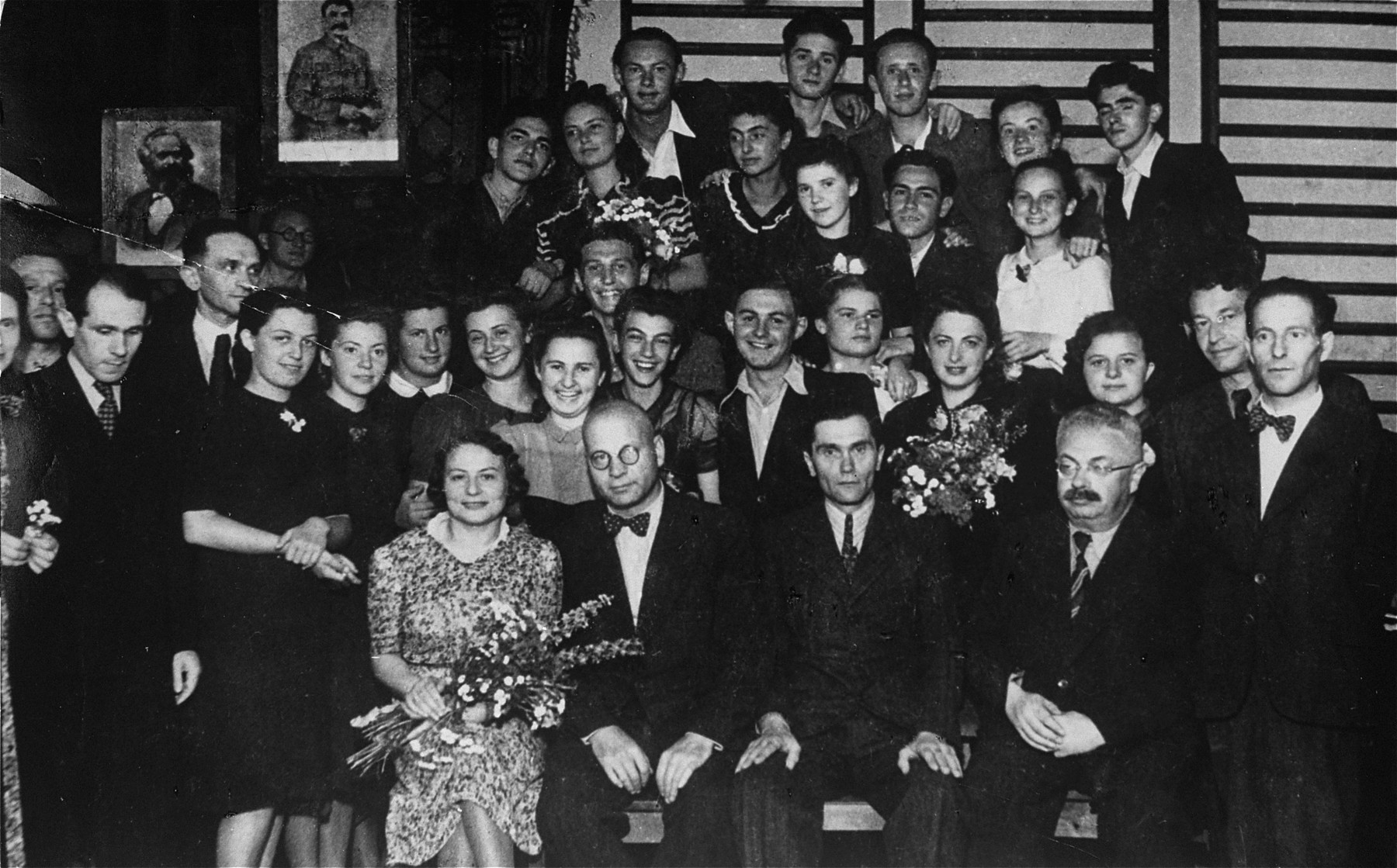 Group portrait of the faculty and graduating class of the Jewish private high school in Drohobycz.

Among those pictured are Bruno Schulz, the Polish author and painter (standing at the left looking down).  Also pictured seated (far left) Mrs. Alter and Jakob Blatt, the principal (far right).  Standing second row, left to right are Bruno Schultz, Mr. Ornstein, unknown, Helena Beck, unknown, unknown, unknown, Tusia Schenkelbach, Ozia Stranzer, Olga Salata, Mrs. Rosberger (nee Harz), Sima Iwaszczenko, Nemlich, Adolph Hirschberg.  Third row: Stempler (?), Ida Hennenfeld, unknown, Rysia Resnick, unknown, and  Lola Oppenheim.  Top row:  Kaiko Kupferberg,  Imek Weiss, Bloch, unknown and a Jewish refugee from Vienna.  Others pictured are Rudek Lanc, and Fredek Koch.