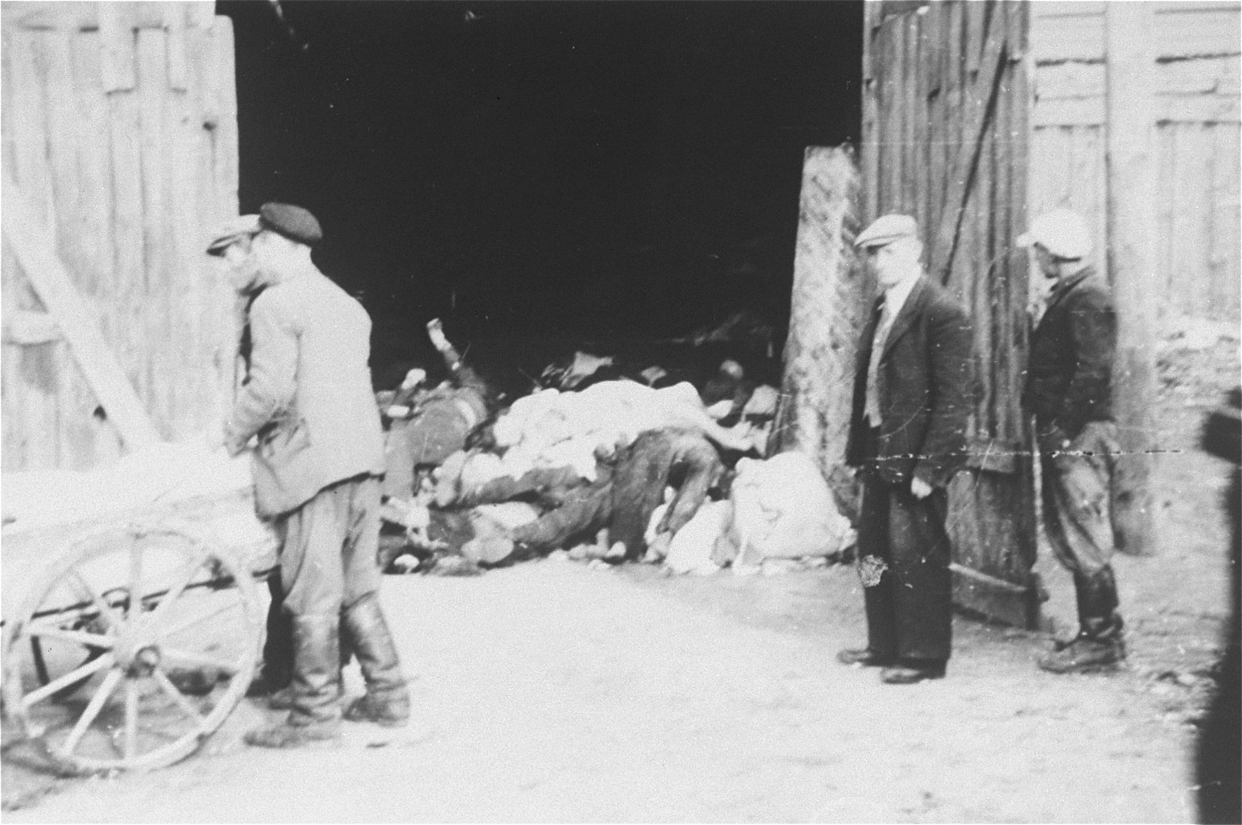 A Jewish council official named Kaminski (right, in front of the door) watches as men remove corpses from a cart and pile them in a barn in the Deblin Irena ghetto.