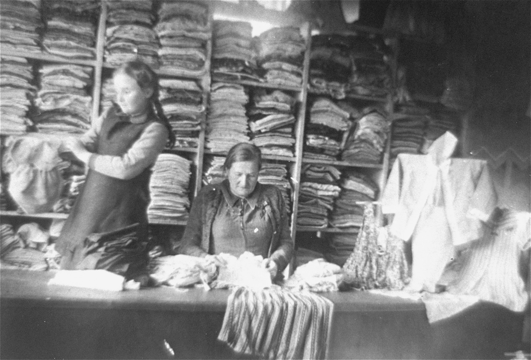 A Jewish woman and girl work in a clothing warehouse in the Glubokoye ghetto.  

Among those pictured is Rajze Lederman.