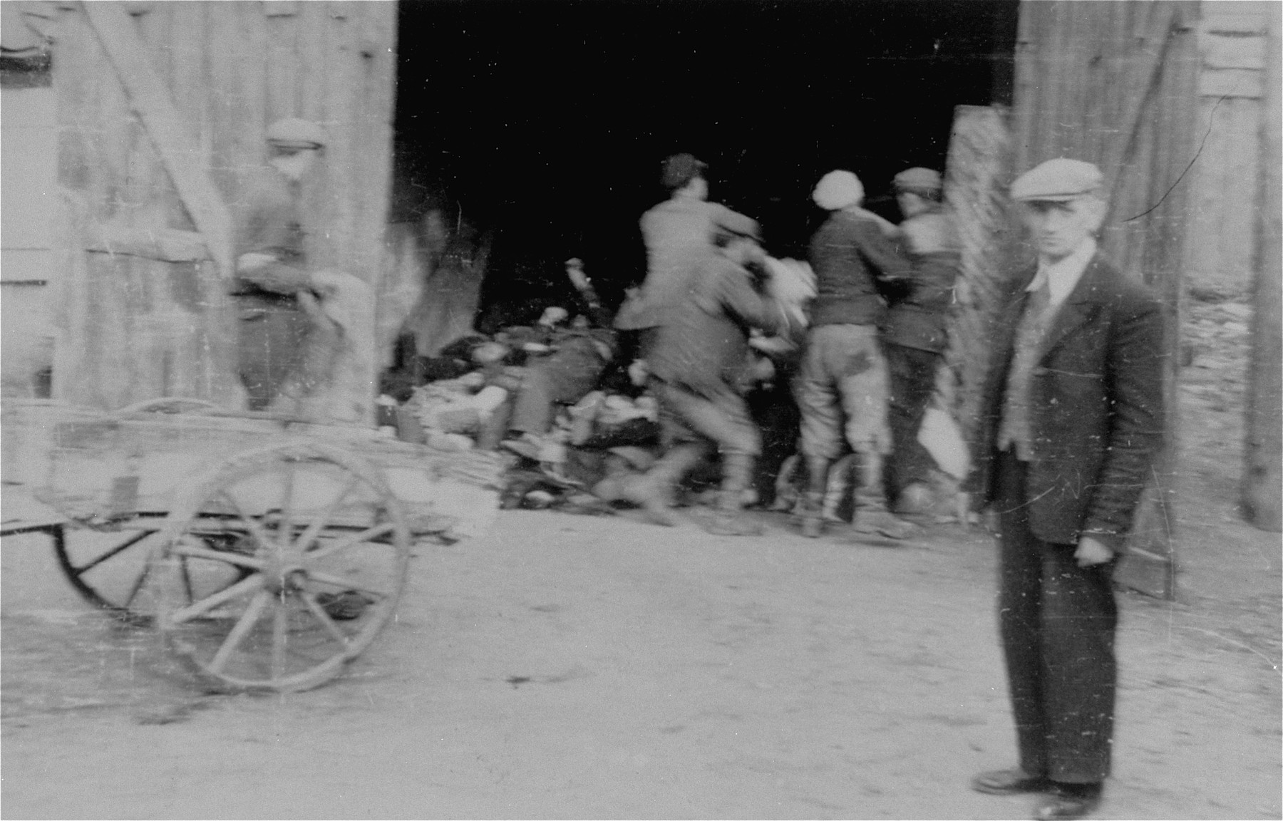 A Jewish council official named Kaminski (in the foreground) watches as men remove corpses from a cart and pile them in a barn in the Deblin Irena ghetto.