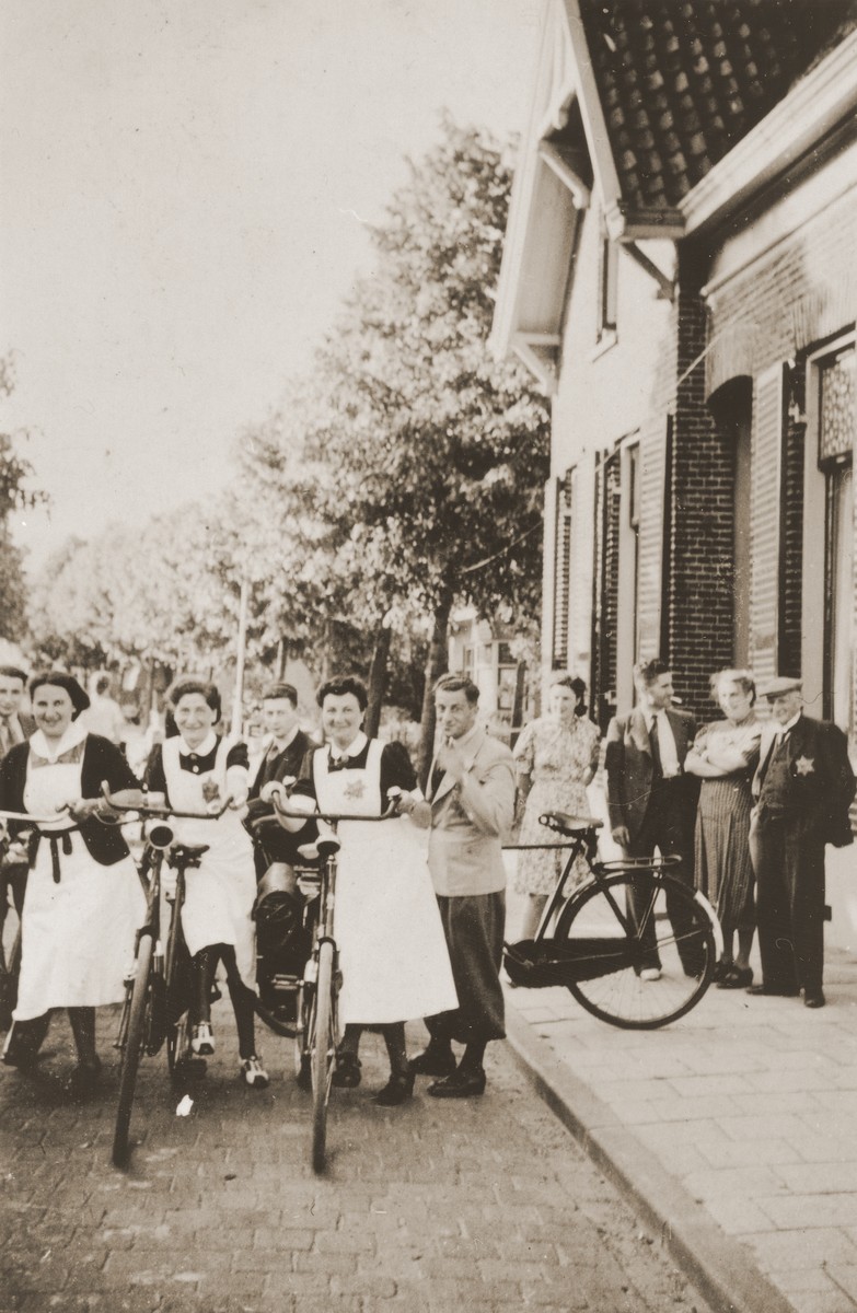 Three Jewish nurses wearing yellow stars are about to begin the 25 mile bicycle ride from their homes in Boekelo to their place of work at the Jewish psychiatric hospital in Apeldoorn [Het Apeldoornse Bos].  Bicycles were their only permitted mode of transport.

The three nurses (from left to right) are Marcelle de Wolff, Gerta Sajet, and Renee Meijer.  Pictured at the far left is Richard Meyer.  In the background at the right (from right to left) are Joseph Meijer, Hennie Meijer, Zadok Zion, and Bep Meijer.