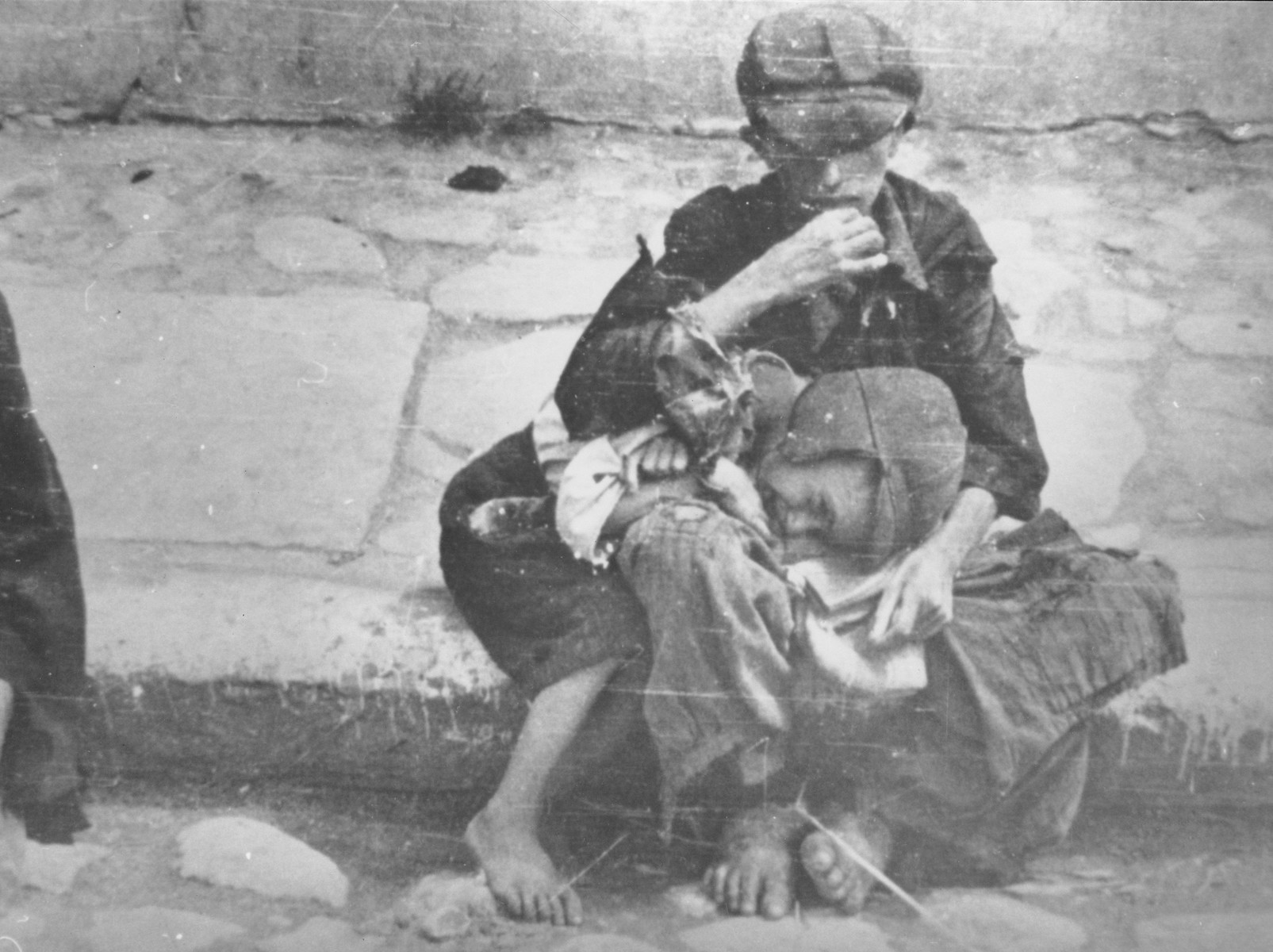 Destitute children sit barefoot on the pavement in the Warsaw ghetto.