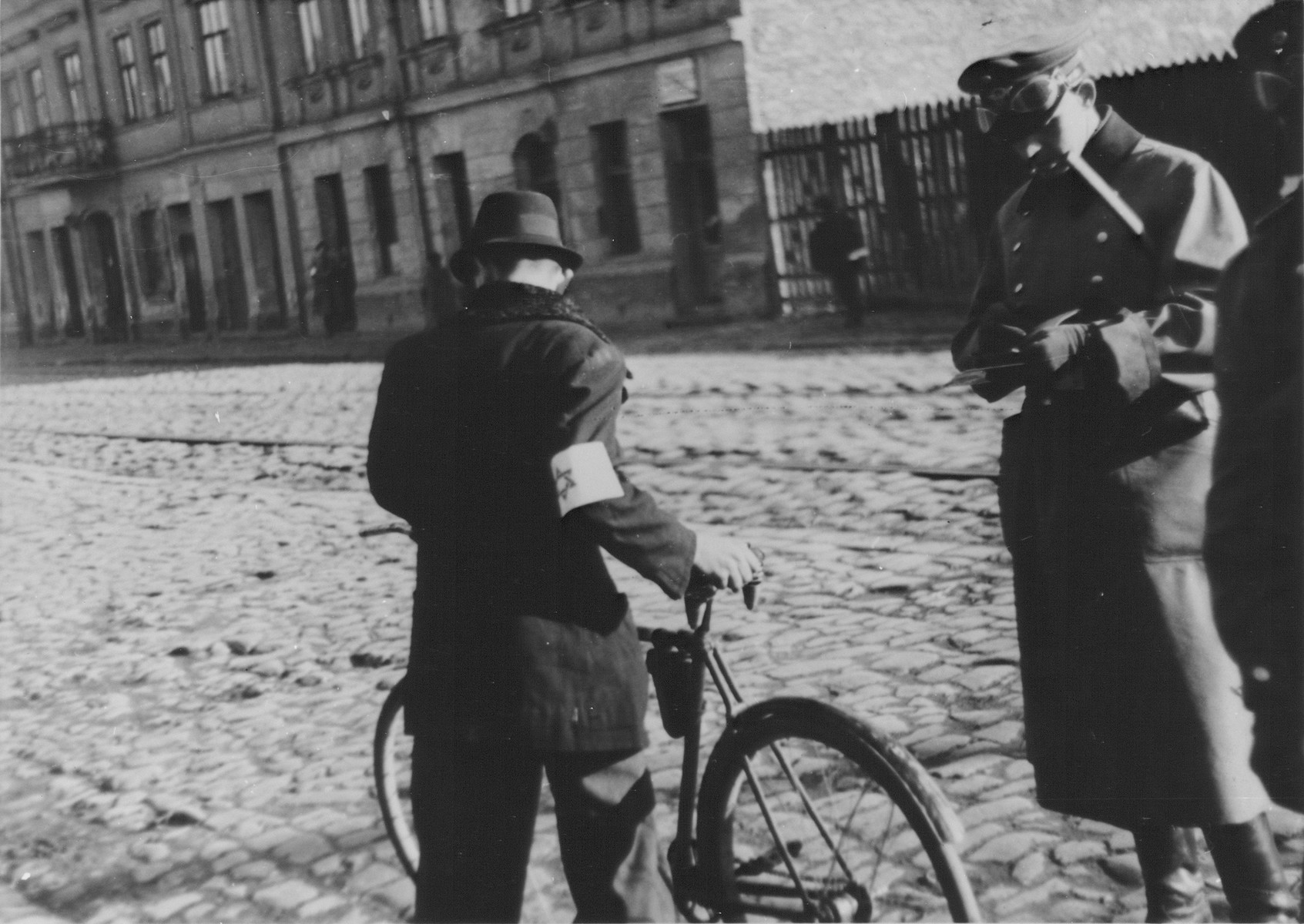 A German policeman checks the papers of a Jewish cyclist on a street in the Warsaw ghetto.