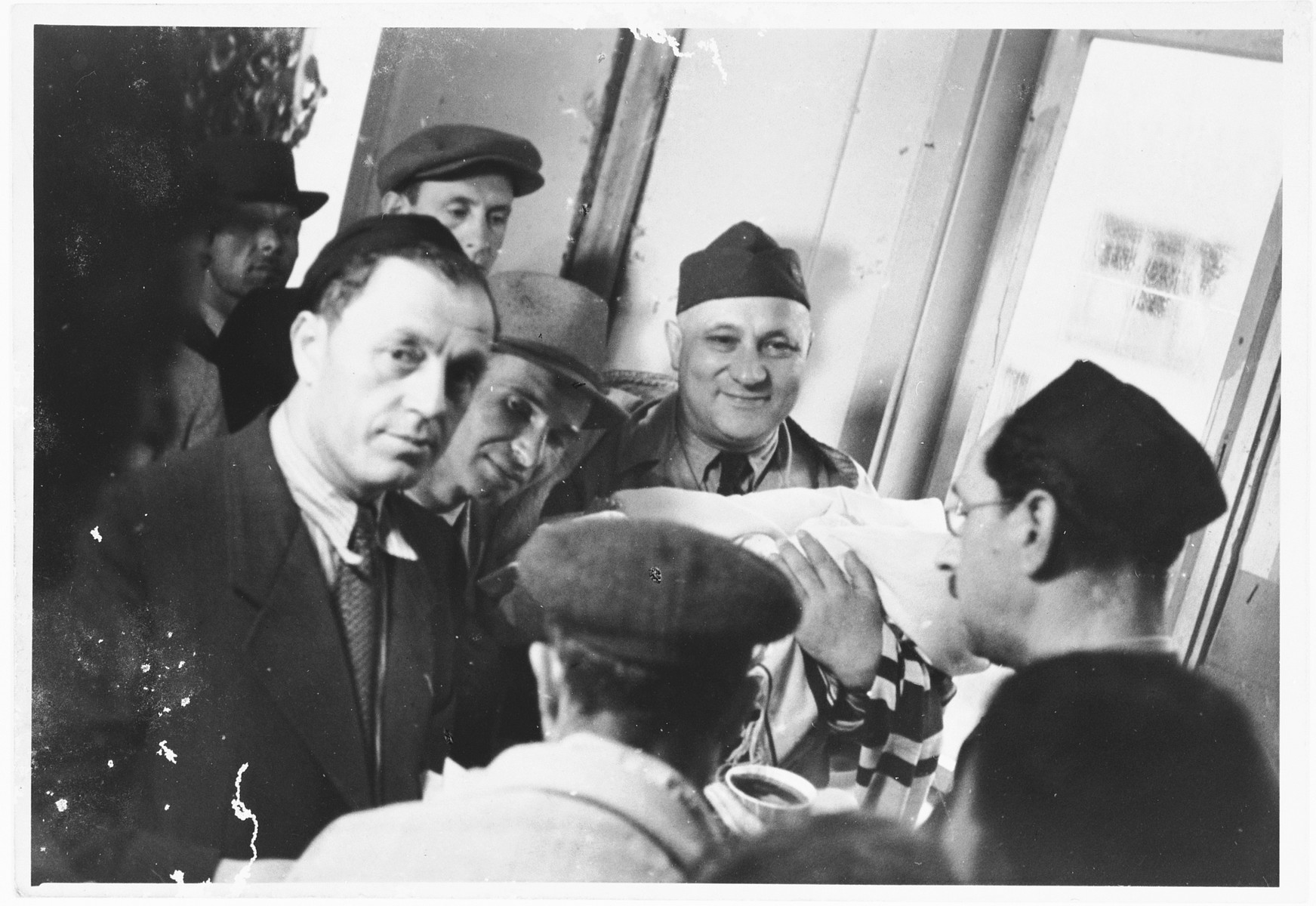 UNRRA camp director Harold Fishbein holds the newborn at a circumcision ceremony in the Schlachtensee displaced persons camp.