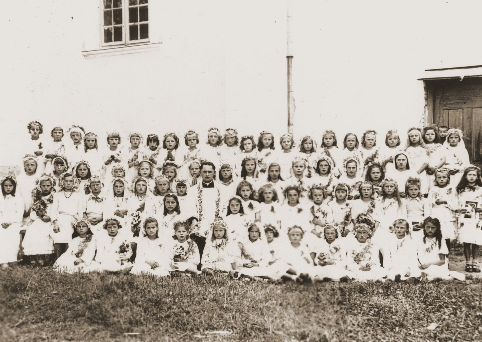 Group portrait of girls at a church school in Wysokie Mazowieckie, Poland, who are dressed for their first communion.  Among the children are twin Jewish sisters who are living in hiding.

The Jewish twins, Celina and Fela Friedmann, are pictured standing in the center of the back row.