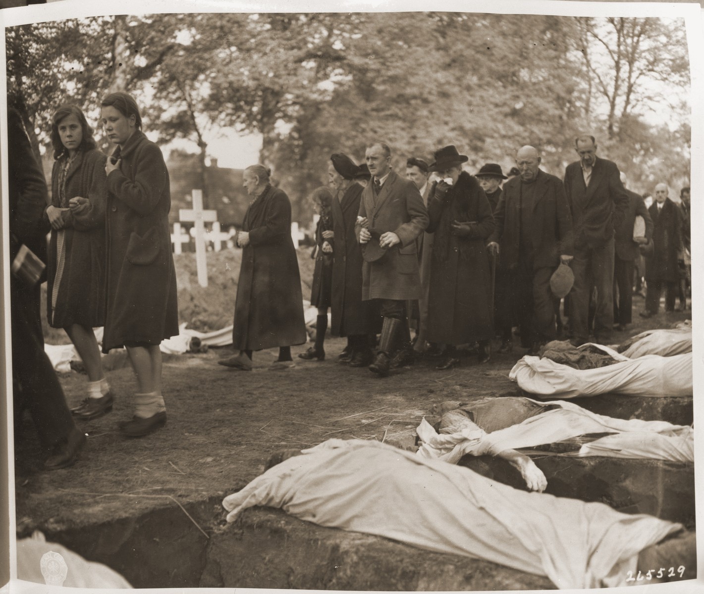 Civilians of all ages are forced to march past the open graves of prisoners from the concentration camp at Woebbelin.  The townspeople were forced by U.S. troops to bury the corpses on the palace grounds of the Archduke of Mecklenburg.