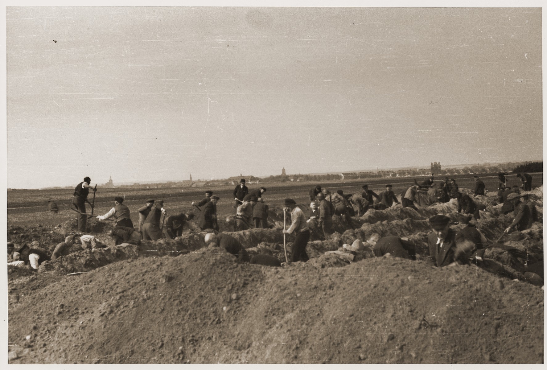 German civilians dig graves for the bodies of concentration camp prisoners killed by the SS in a barn just outside of Gardelegen, which can be seen in the background.
