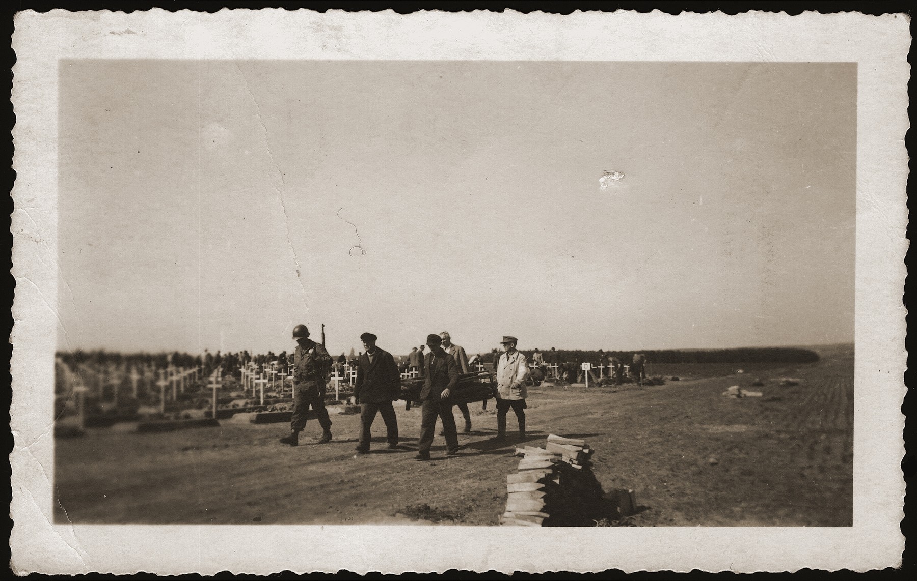 Under the supervision of an American soldier, German civilians carry stretchers past the cemetery containing concentration camp prisoners killed by the SS in a barn outside of Gardelegen.