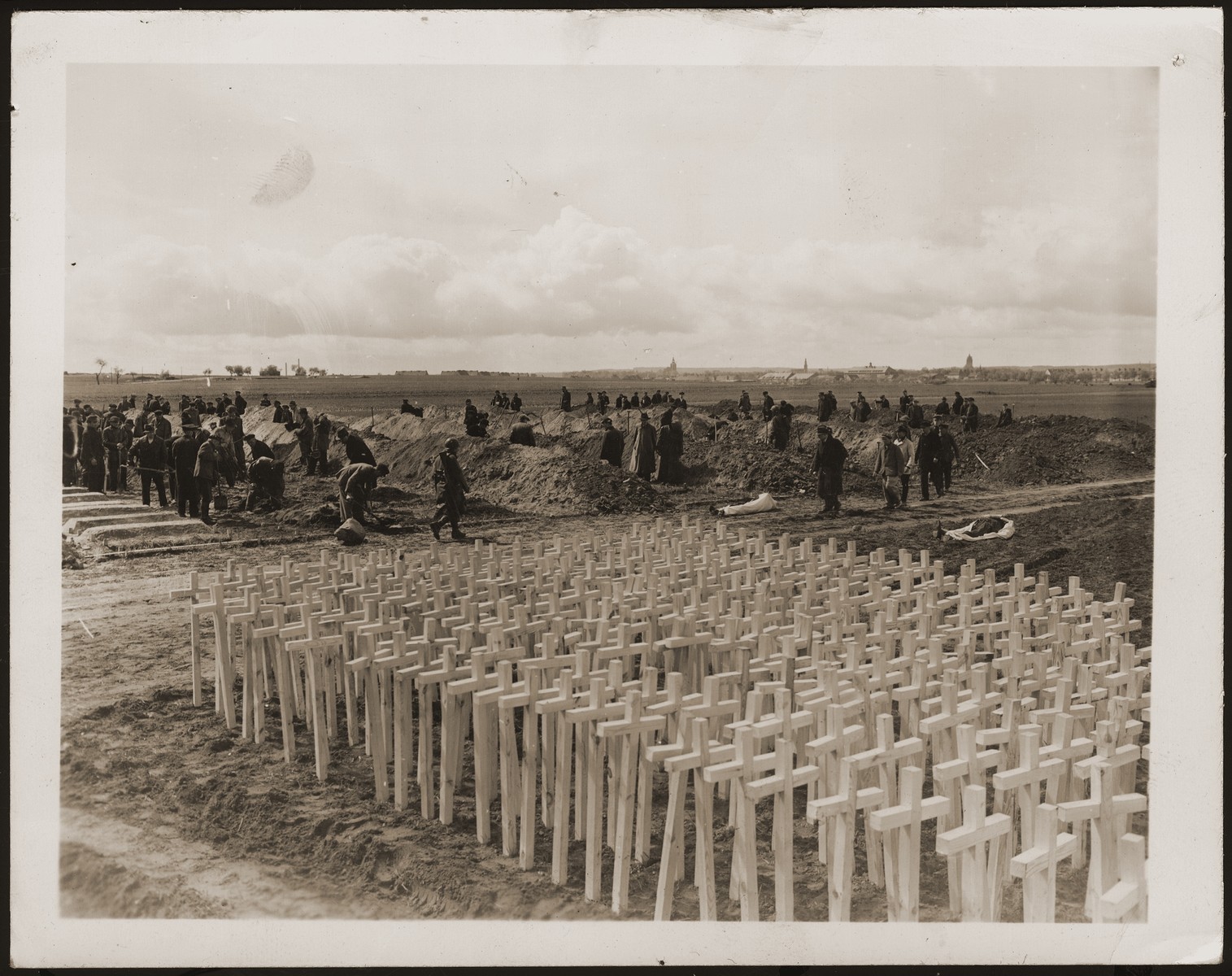 Under the supervision of American soldiers, German civilians dig graves for the bodies of concentration camp prisoners killed by the SS in a barn just outside of Gardelegen.  In the foreground are grave markers that will be placed on the graves.