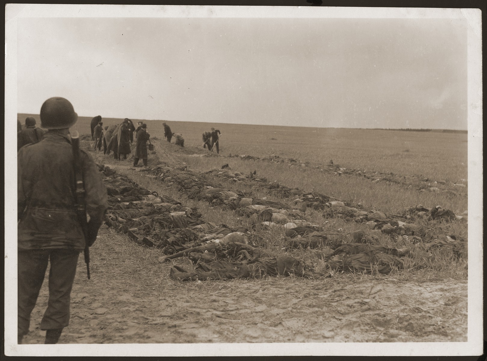 Under the supervision of American soldiers, German civilians from Gardelegen dig graves for the bodies of prisoners killed by the SS in a barn just outside the town.